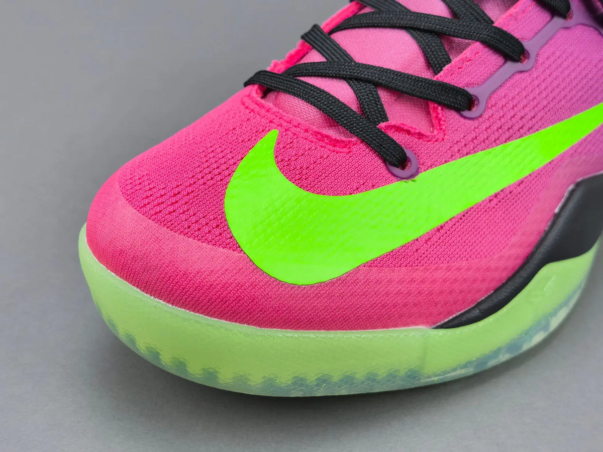 Close-up of a Nike sneaker in bright pink and neon green, showing the side logo, black laces, and a translucent green outsole on a gray background.
