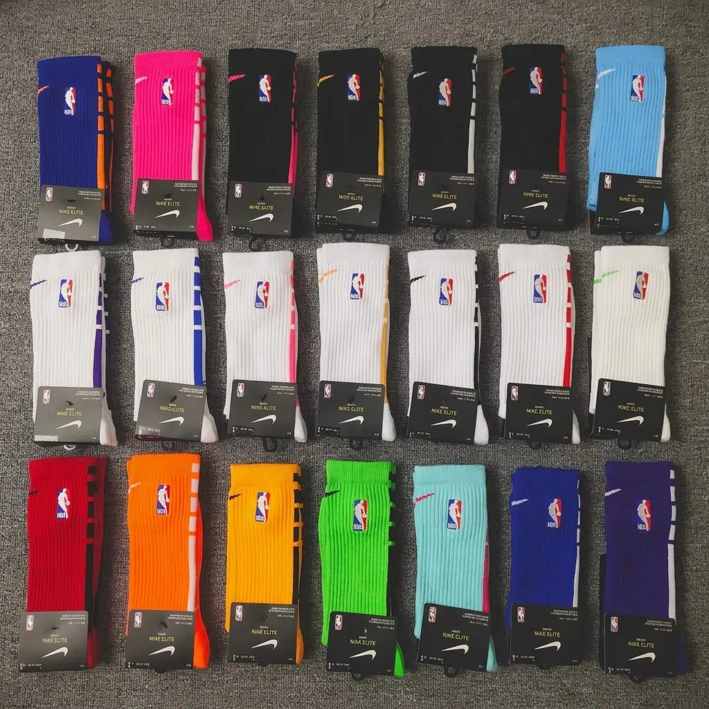 Twenty pairs of Nike NBA crew socks arranged in five rows of four on a gray carpet. The socks come in multiple colors including blue, pink, black, orange, white, red, green, and purple, each with its corresponding NBA team logo and Nike swoosh visible.