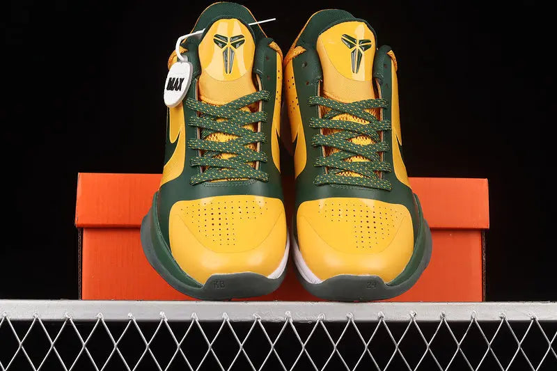 A pair of yellow and green Nike basketball sneakers displayed on top of an orange shoebox against a black background.