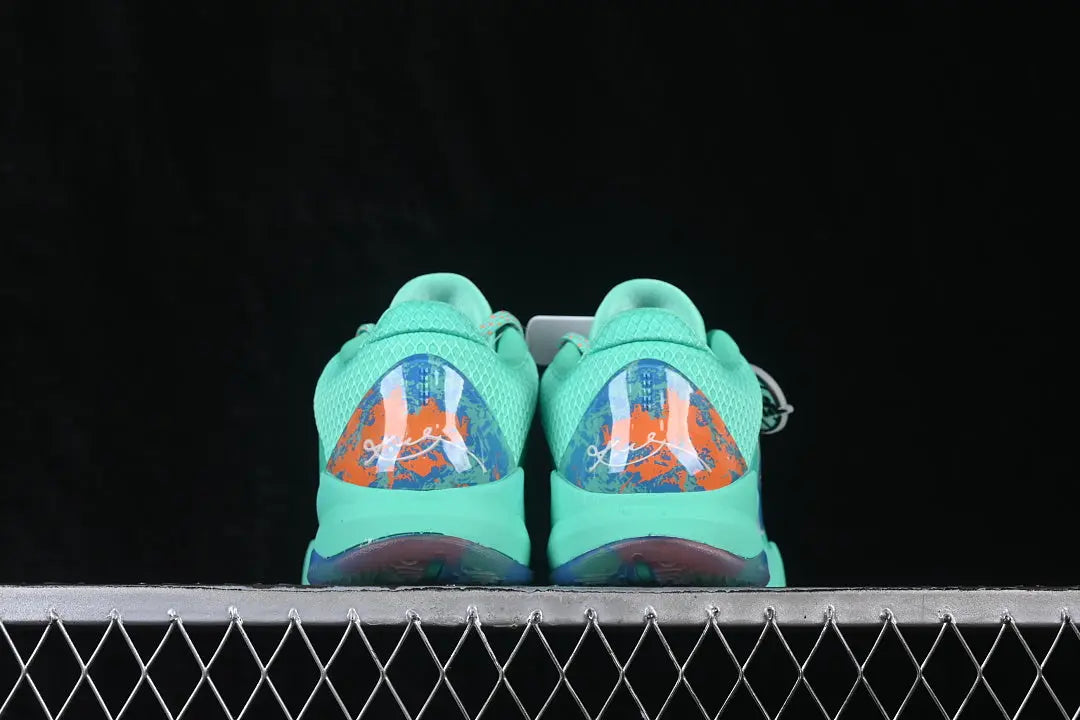 A pair of mint green and orange basketball sneakers shown from the back, resting on a metal grid against a black background.