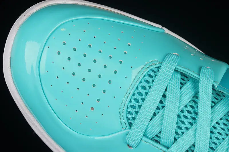 A close-up of a turquoise athletic shoe showing the toe box, perforated synthetic upper, mesh side panel, and matching laces against a black background.