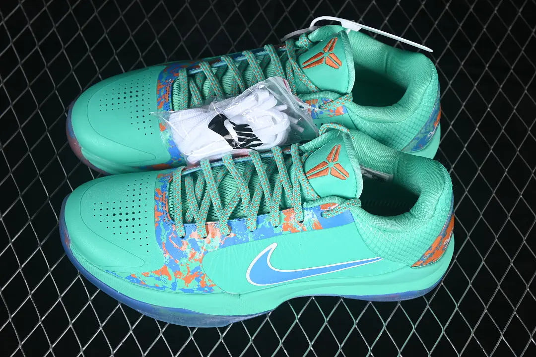 A pair of Nike basketball shoes in a vibrant mint green colorway, featuring a blue and orange abstract pattern on the sides, a blue Swoosh, and white laces, displayed on a black chain-link fence background.