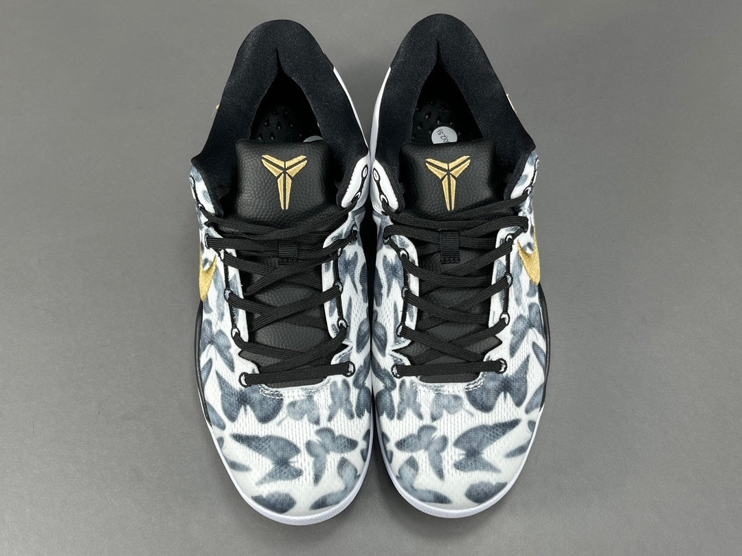 Pair of black and white sneakers with a gold logo on a gray background