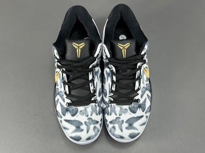Pair of black and white sneakers with a gold logo on a gray background