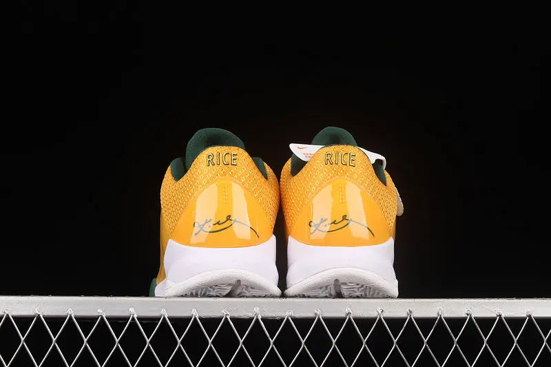 A pair of yellow and green sneakers shown from the back, resting on a white metal grid against a solid black background. The word 'RICE' is printed on the heel area.