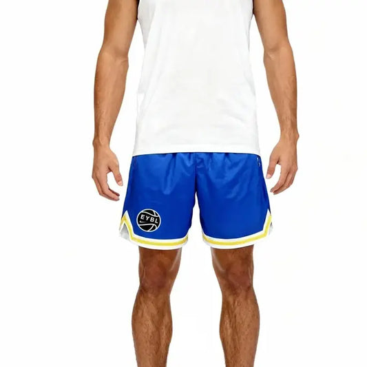 A man wearing blue athletic shorts with yellow and white trim, featuring a circular black and white logo on the left leg, paired with a white tank top against a plain white background.