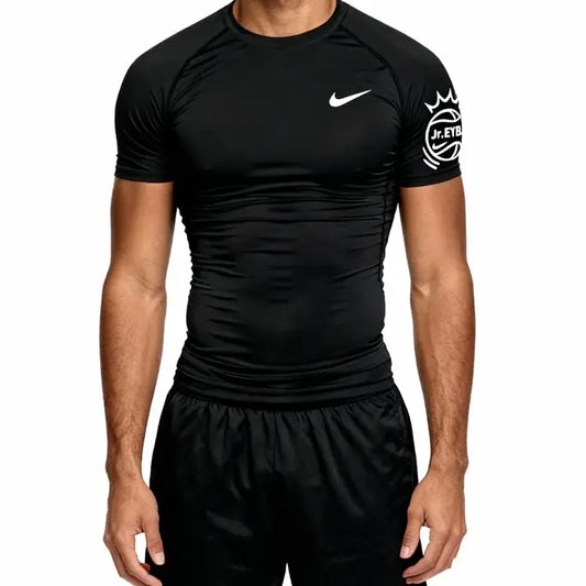 A man wearing a black Nike athletic compression shirt with a white swoosh logo on the chest and a white crest graphic on the sleeve, paired with black shorts, against a plain white background.