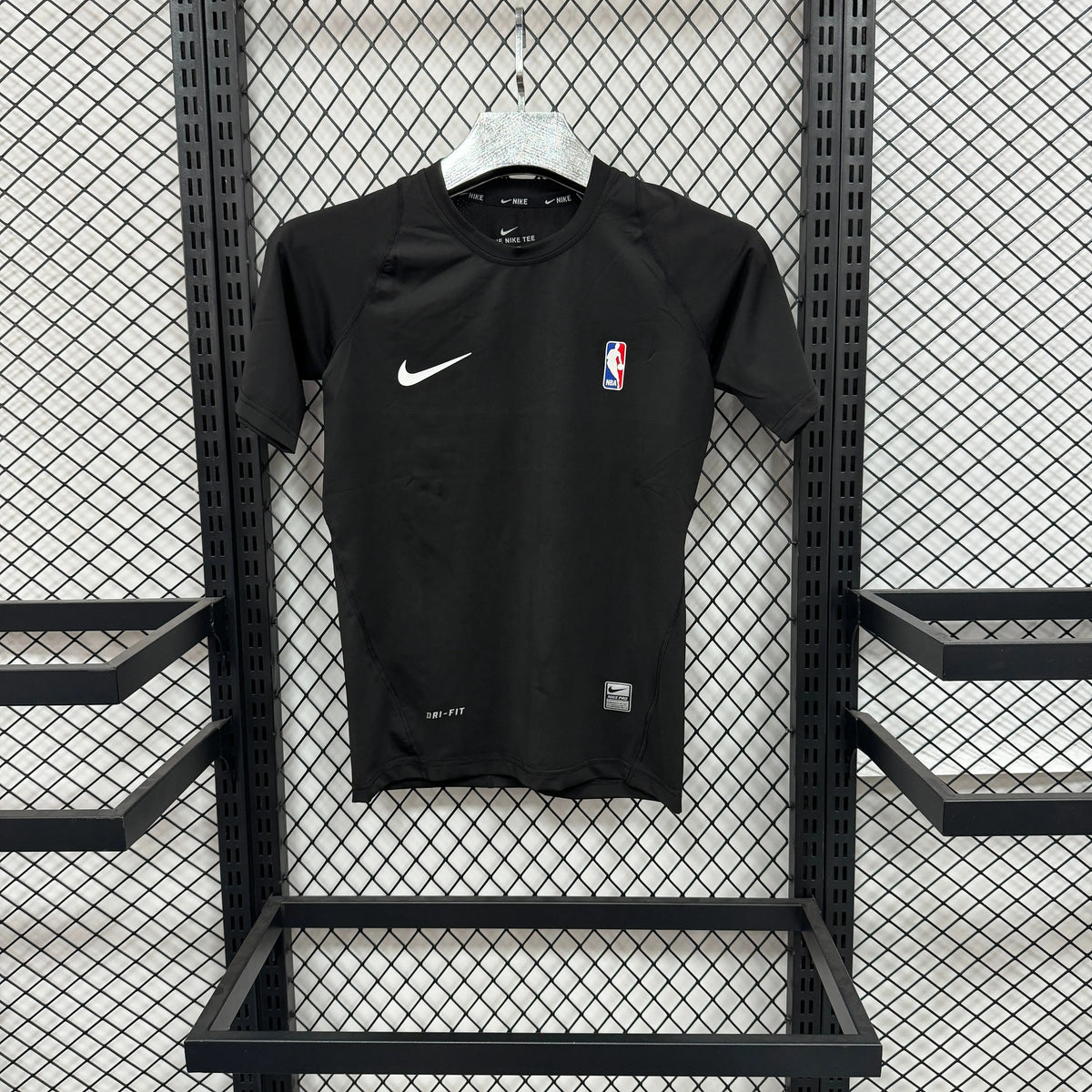 A black Nike short-sleeve athletic t-shirt with a white swoosh and NBA logo, hanging on a white hanger against a black metal mesh display rack.
