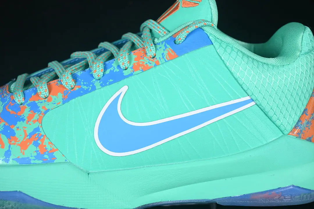 A close-up of a Nike athletic shoe in mint green, light blue, and orange, showing the side profile with the Nike Swoosh logo.