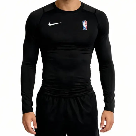 A man wearing a black long-sleeve athletic compression shirt with a white Nike swoosh on the right chest and an NBA logo on the left chest, paired with black athletic shorts, against a plain white background.