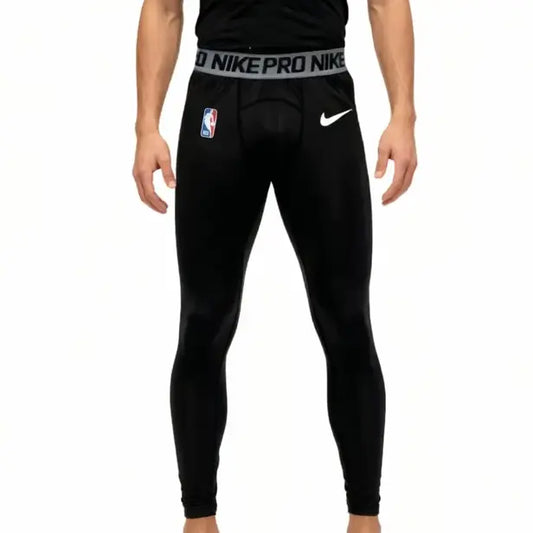 Black Nike Pro basketball tights worn by a model, featuring a white Nike logo on the right thigh, an NBA logo on the left thigh, and a white Nike Pro waistband.