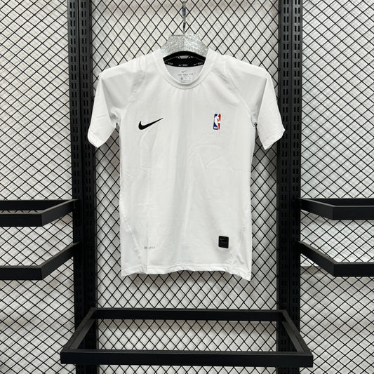 A white Nike short-sleeve athletic jersey with a black swoosh on the right chest and an NBA logo on the left chest, hanging on a hanger against a black metal mesh display wall.