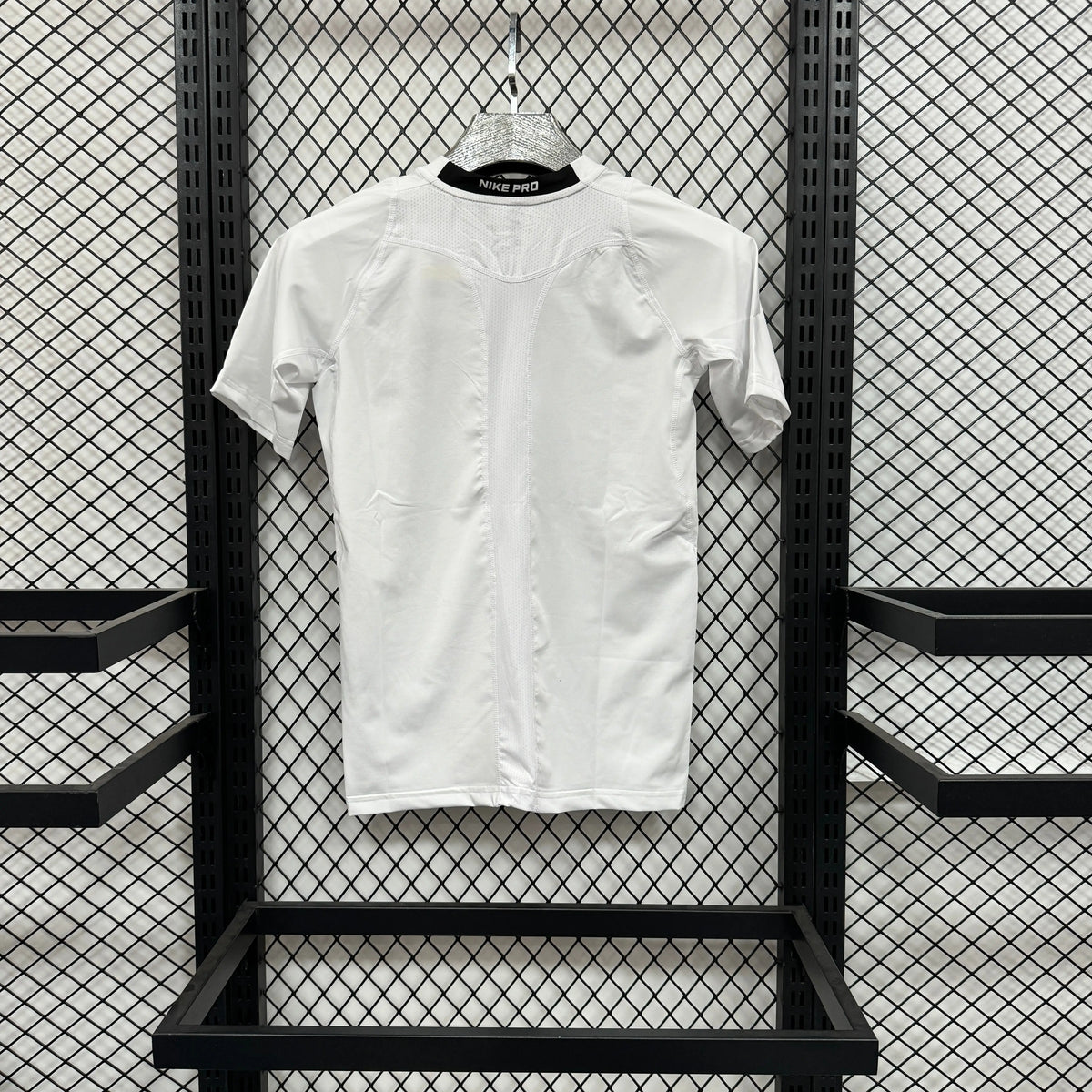 A white short-sleeve button-front t-shirt with decorative pleated detailing on the shoulders, hanging on a hanger against a black metal mesh display rack.