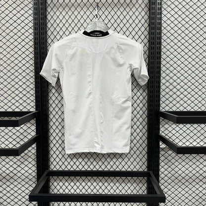 A white short-sleeve button-front t-shirt with decorative pleated detailing on the shoulders, hanging on a hanger against a black metal mesh display rack.