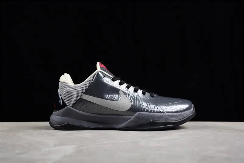 A Nike basketball shoe in metallic silver and dark gray with a white Swoosh, shown from the side against a black background and light gray surface.