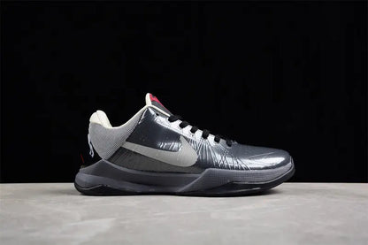 A Nike basketball shoe in metallic silver and dark gray with a white Swoosh, shown from the side against a black background and light gray surface.