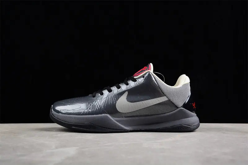 A Nike basketball shoe in metallic dark gray and silver with a white Swoosh, black laces, and a small red accent on the tongue and heel, displayed on a gray surface against a black background.