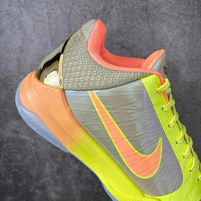 A close-up of a Nike basketball shoe featuring a metallic silver textured upper, a bright neon yellow and orange gradient midsole, and a prominent orange Nike Swoosh.