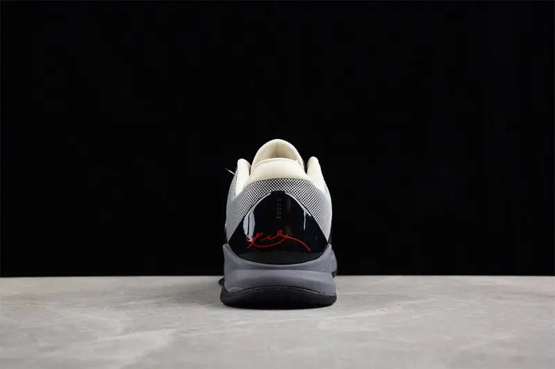 A single sneaker shown from the rear, featuring a white and gray mesh upper, a glossy black heel counter with a red script logo, and a gray and black sole, set against a dark background.