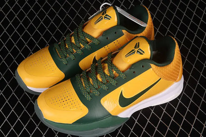 A pair of Nike basketball sneakers in yellow and green, featuring a Kobe Bryant logo on the tongue and a green Nike swoosh on the side, displayed on a black wire mesh background.