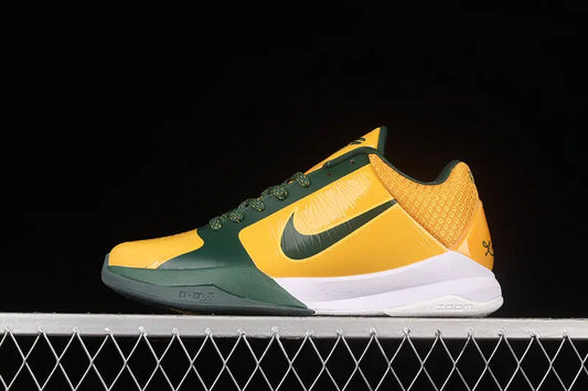 A Nike athletic shoe in yellow and dark green with a white midsole, photographed in profile against a black background with a white wire grid at the bottom.