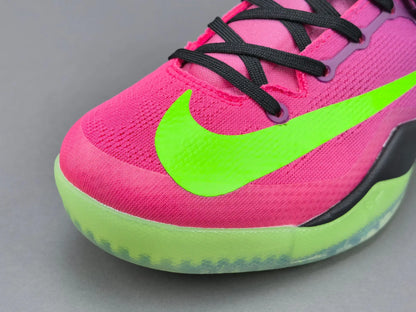 Close-up of a Nike sneaker in bright pink and neon green, showing the side logo, black laces, and a translucent green outsole on a gray background.
