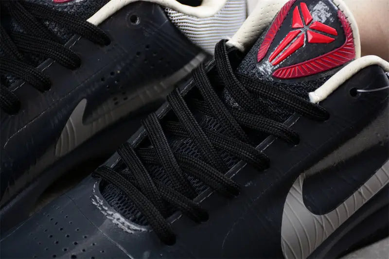 Close-up of a black Nike sneaker with black laces, a red and black tongue logo, and a light gray Swoosh on a dark background.