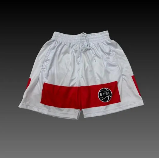 White athletic shorts with a bold red horizontal stripe across the lower front and a circular black, white, and red EYBL logo patch. The shorts feature an elastic waistband with a drawstring and are shown against a dark gray gradient background.