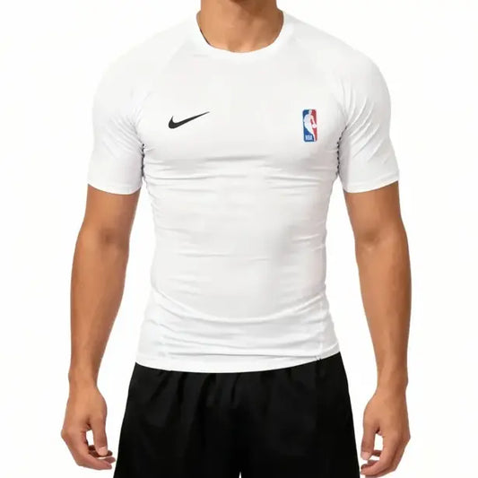 A man wearing a white Nike short-sleeve athletic compression shirt with a black swoosh on the right chest and an NBA logo on the left chest, paired with black shorts.