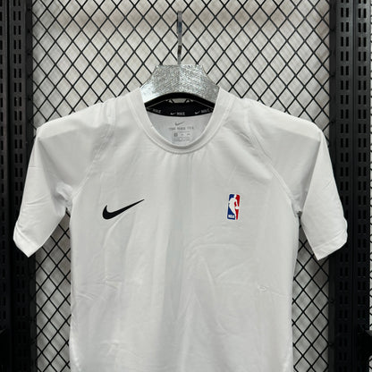 A white Nike short-sleeve athletic jersey hanging on a silver hanger against a black metal mesh backdrop. The jersey features a black Nike swoosh on the right chest and an NBA logo on the left chest.