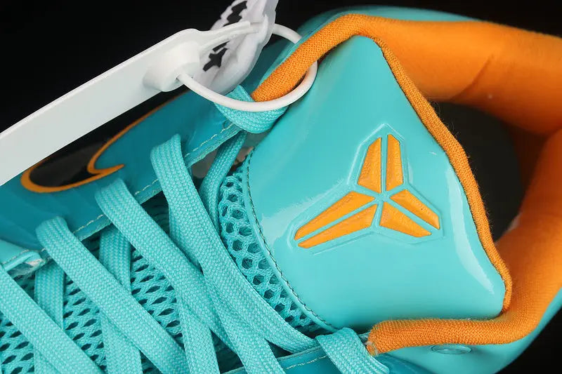 Close-up of a basketball sneaker featuring a bright turquoise blue leather upper with an orange Kobe Bryant logo on the tongue, orange lining, and matching turquoise laces.
